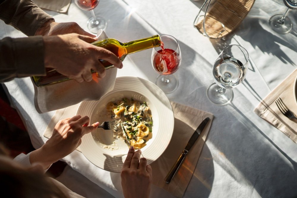 Imagen de una experiencia de fine dining, donde se sirve pasta en un plato elegante mientras se vierte vino en una copa, con un ambiente sofisticado y atención al detalle.